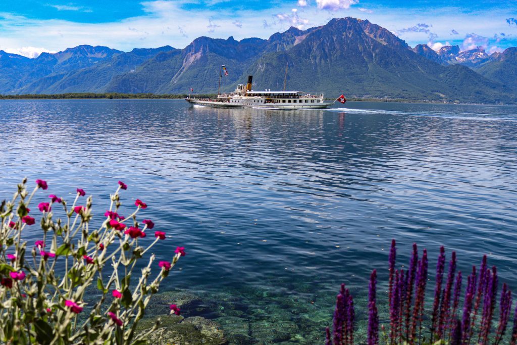 Historisches Schiff fährt über den weiten See vor hohen Bergen und blauem Himmel.