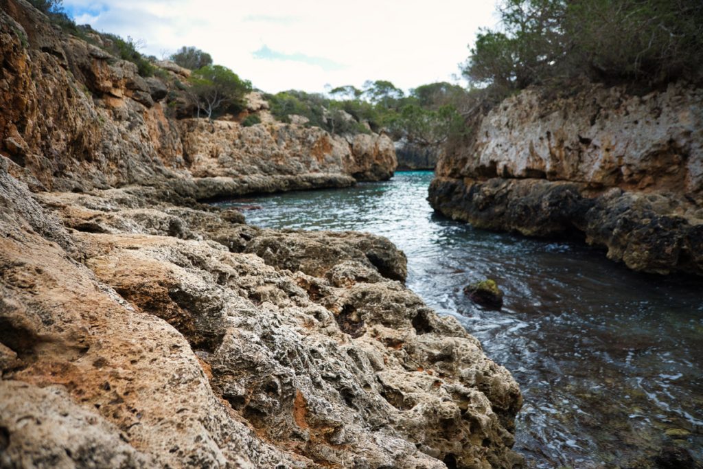 Nahaufnahme der zerklüfteten Felsen einer engen Küstenbucht mit sanften Wellen.