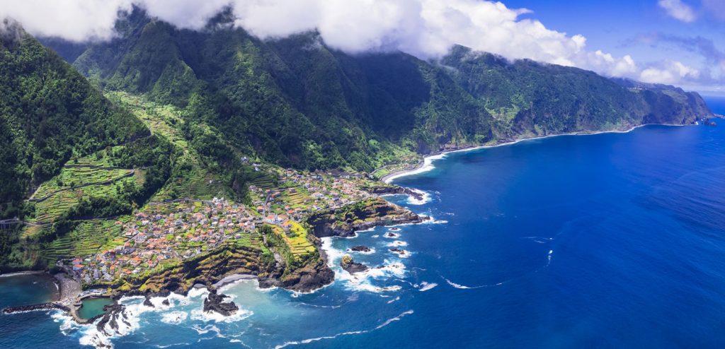 Luftbild zeigt grüne Steilhänge, Felsterrassen und Siedlungen am Atlantik.