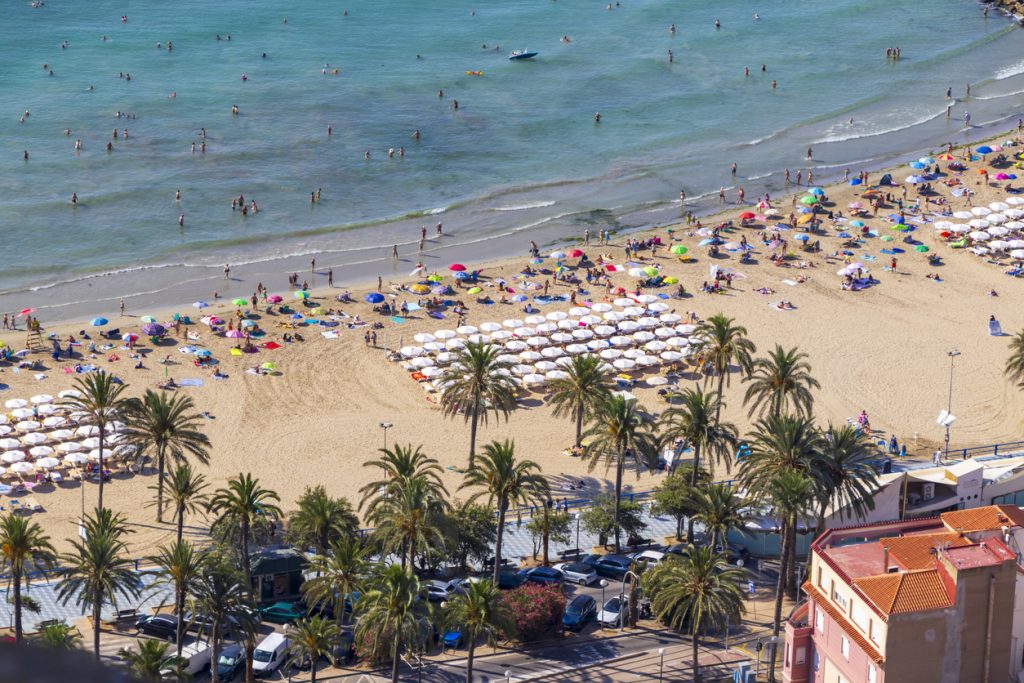 Breiter Sandstrand bei Alicante mit Promenade, Sonnenschirmen und vielen Badegästen.