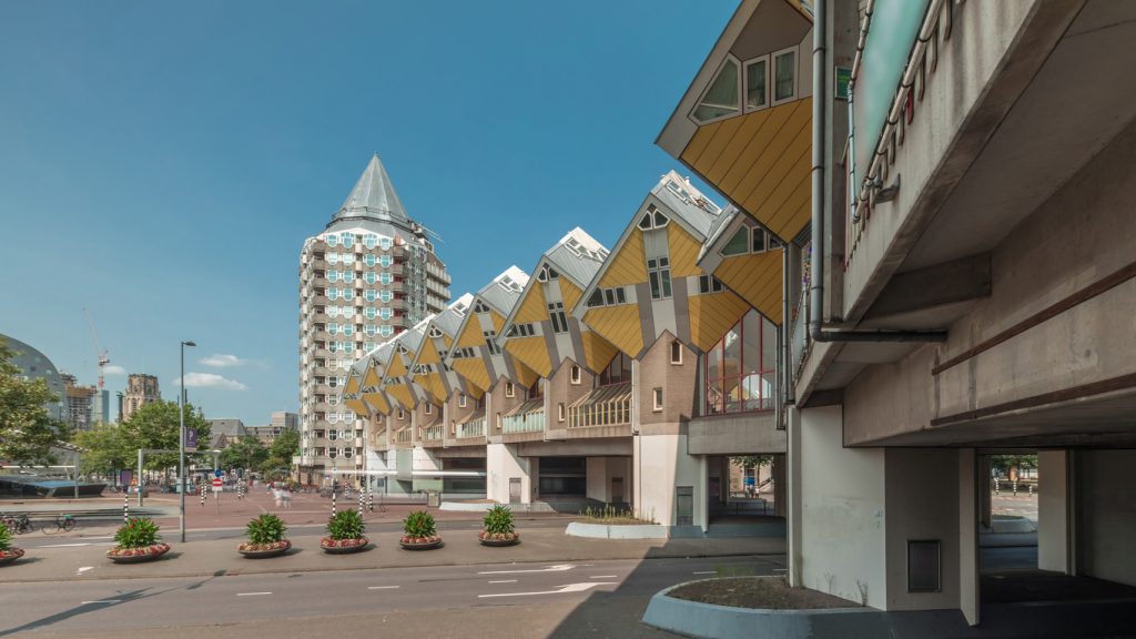 Gelbe Kubushäuser in Rotterdam mit dem Bleistift Turm vor blauem Himmel.