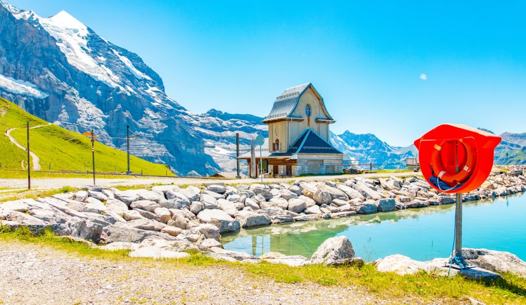 Kleines Berghaus steht an einem türkisfarbenen See unter hohen Gletscherbergen.