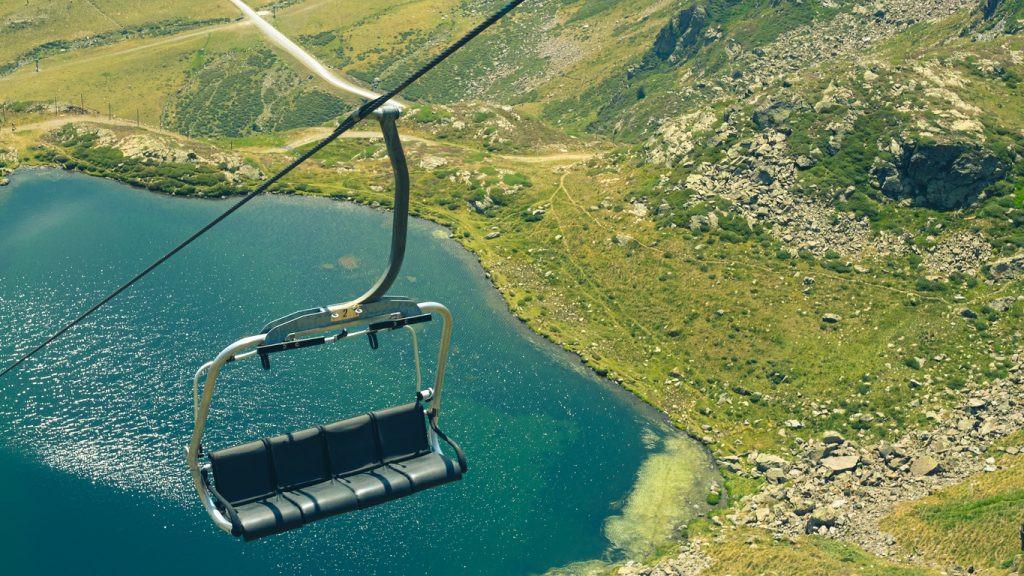 Ein leerer Sessellift schwebt über einem tiefblauen See in den Pyrenäen.