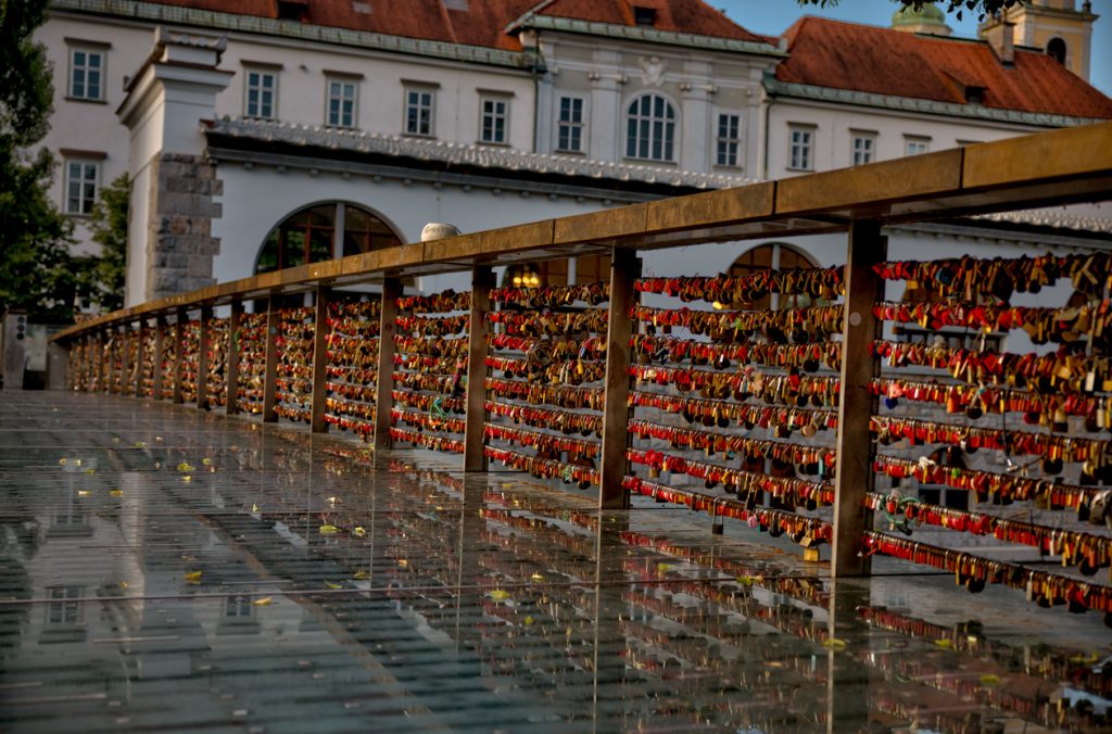 Glasbrücke mit dichten Reihen bunter Vorhängeschlösser vor alten Häusern.