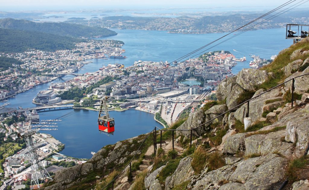 Rote Gondel schwebt über Bergen mit Blick auf Stadt und Fjorde.