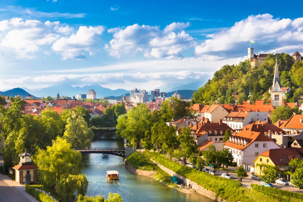 Blick auf Fluss, Brücken, rote Dächer und Burg mit Bergen im Hintergrund.