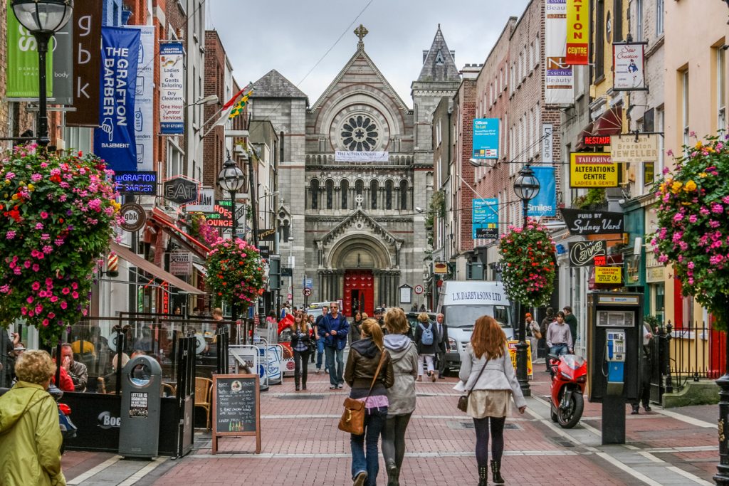 Fußgängerzone in Dublin mit Cafés, Blumenampeln und St. Ann’s Church.