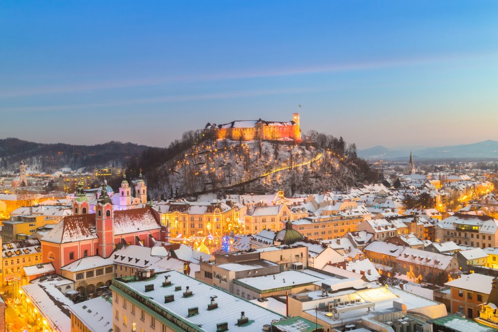 Winterliches Stadtpanorama mit erleuchteter Burg auf einem Hügel.