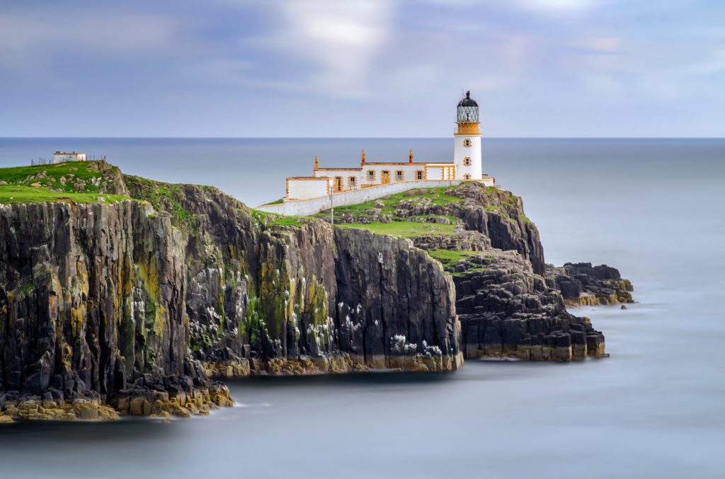 Weißer Leuchtturm auf grüner Klippe am ruhigen Meer der Isle of Skye.