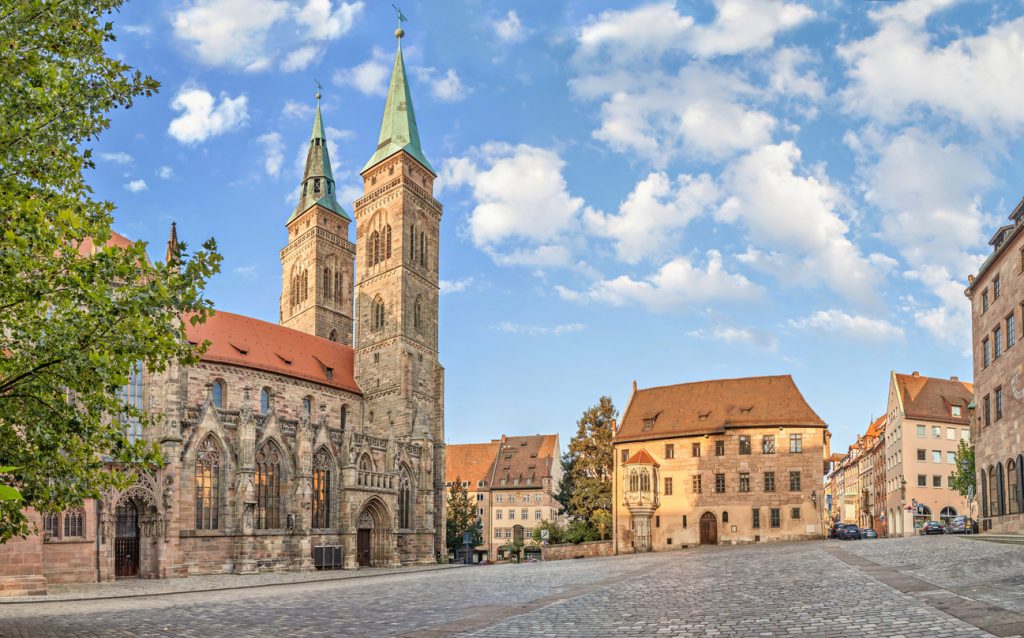 Die romanisch-gotische Sebalduskirche mit ihren Doppeltürmen steht an einem weiten Platz im warmen Licht.