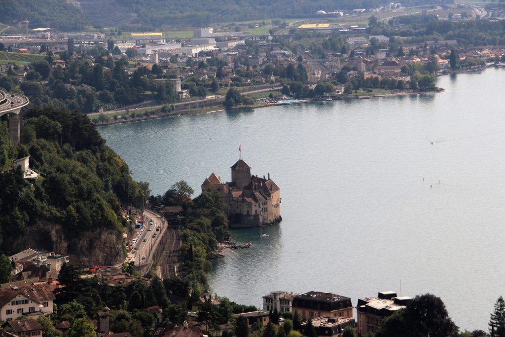 Luftaufnahme von Schloss Chillon am Ufer des Genfersees mit Straße und Bahnlinie daneben.