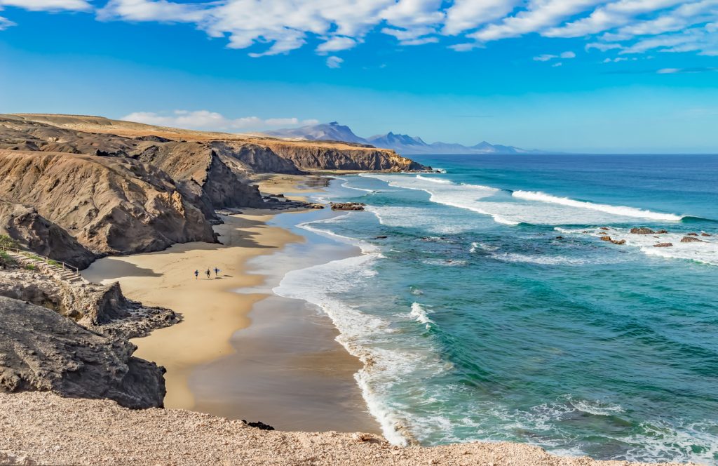 Blick von oben auf eine lange Bucht mit Felsen, Sand und türkisblauem Meer auf Fuerteventura.