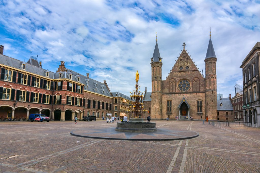 Blick über den Binnenhof mit Brunnen und gotischer Fassade in Den Haag unter wolkigem Himmel.