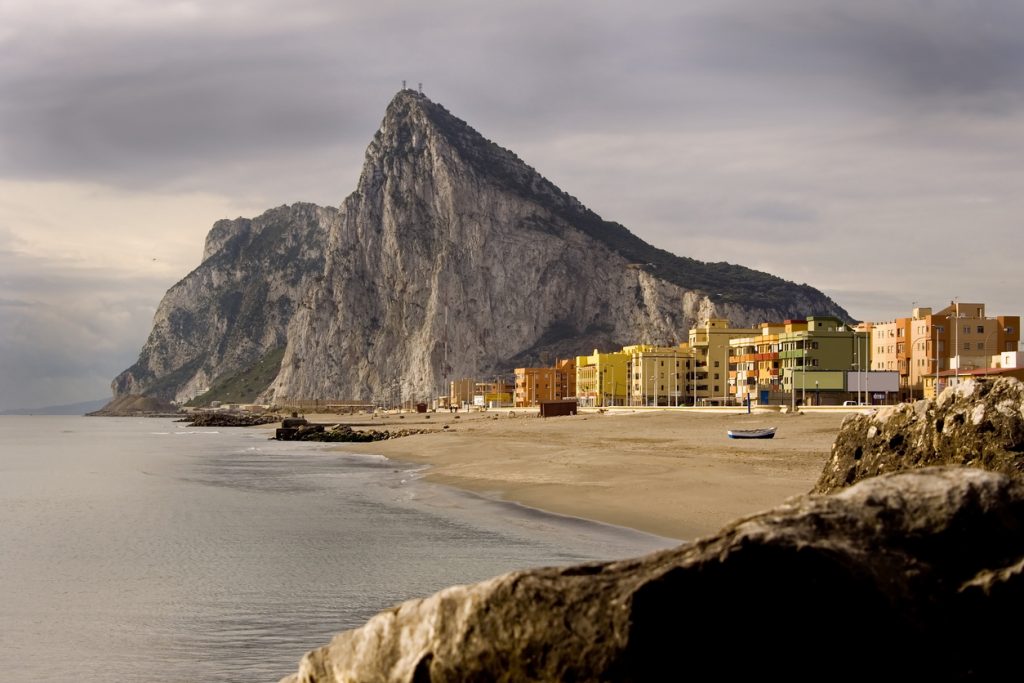 Küste am Fuß des Felsens von Gibraltar mit bunten Häusern und breitem Sandstrand.