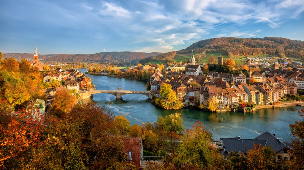 Bunte Altstadt mit Brücke liegt an einem Fluss in herbstlicher Schwarzwaldlandschaft.
