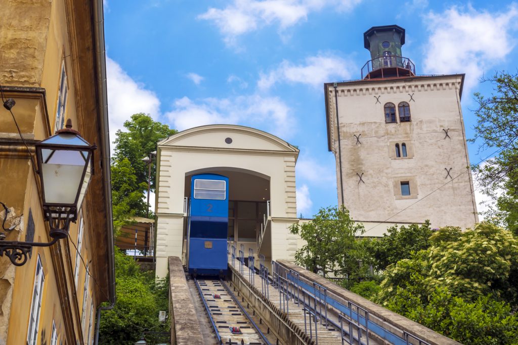 Blaue Standseilbahn fährt in Zagreb zur Oberstadt hinauf, daneben steht der Lotrščak-Turm.