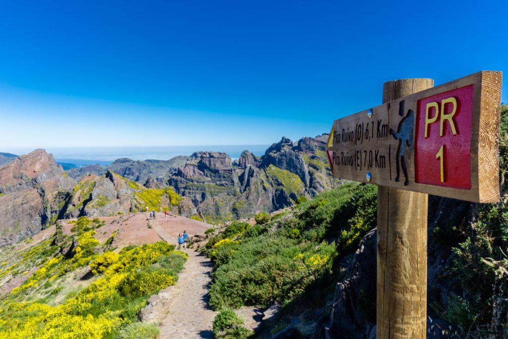in Wegweiser am PR1 zeigt den Pfad vom Pico do Areeiro zum Pico Ruivo auf Madeira vor schroffen Bergen.