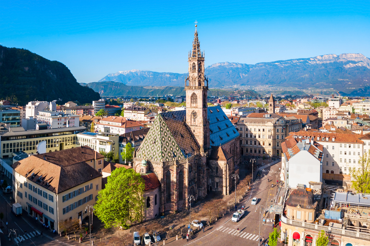 Gotischer Dom mit bunt gemustertem Dach inmitten der Stadt vor Bergen.