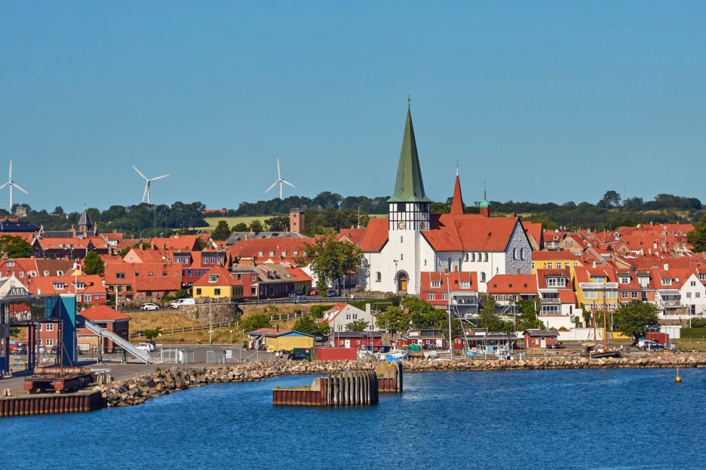 Panorama einer Küstenstadt auf Bornholm mit markanter Kirche und Windrädern im Hintergrund.
