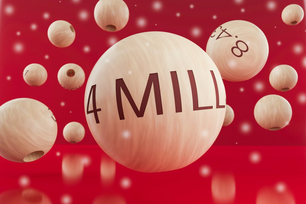 Nahaufnahme einer Holz-Lotokugel mit der Aufschrift „4 MILL“ vor roten Hintergrund, Symbol für den Hauptgewinn von El Gordo.