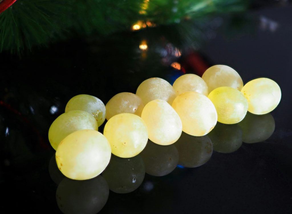 Zwölf helle Weintrauben liegen auf einer glänzend schwarzen Fläche als Symbol für Silvester auf Mallorca.