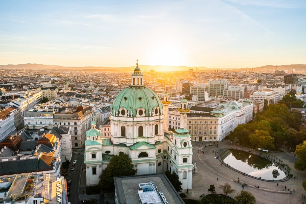 Luftaufnahme der Karlskirche in Wien bei untergehender Sonne und Blick über die Stadt.