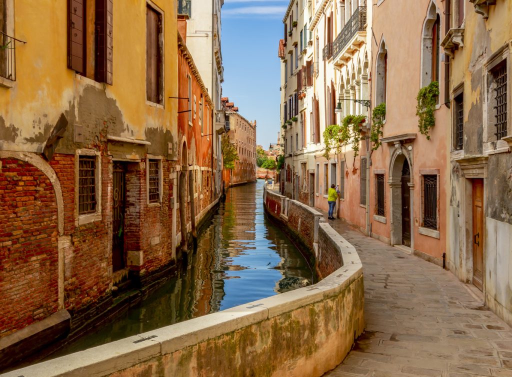 Schmale Gasse mit Wohnhäusern und einem ruhigen Kanal in Venedig bei Sonnenschein.