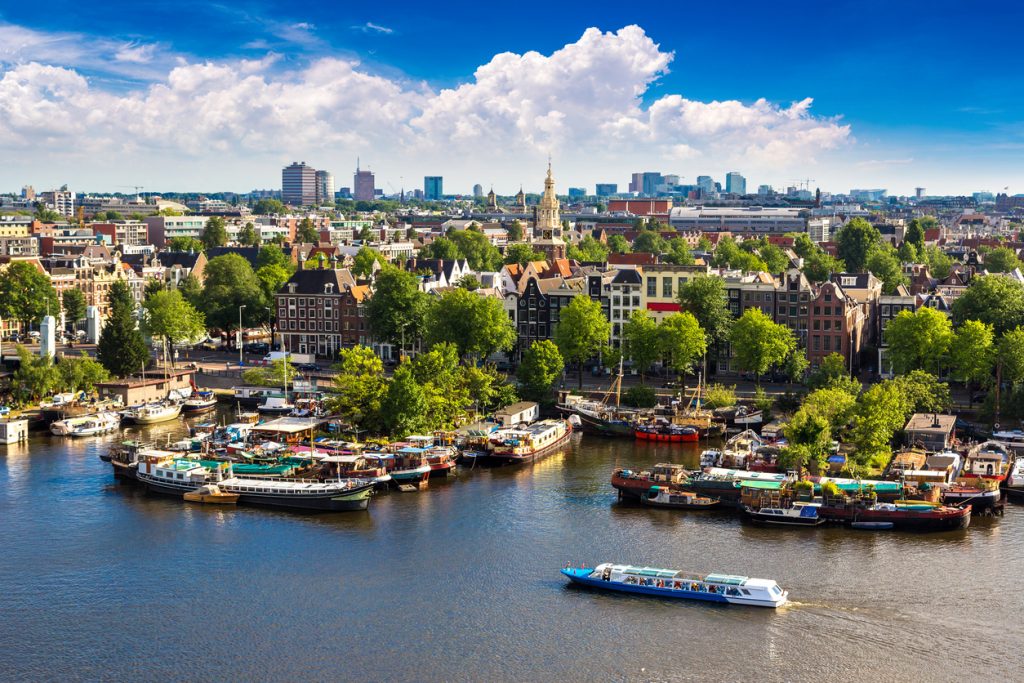 Panorama von Amsterdam mit vielen Booten am Wasser und der Skyline unter großen Wolken.