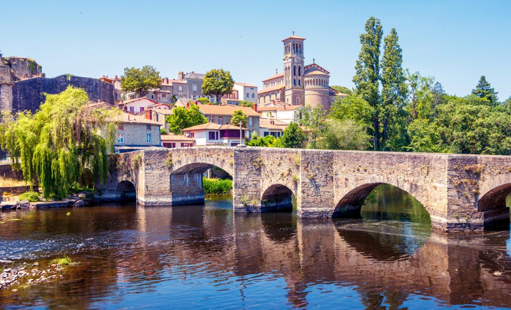 Eine alte Steinbrücke überspannt in Clisson bei Nantes den Fluss, dahinter liegen Kirche und historische Häuser.