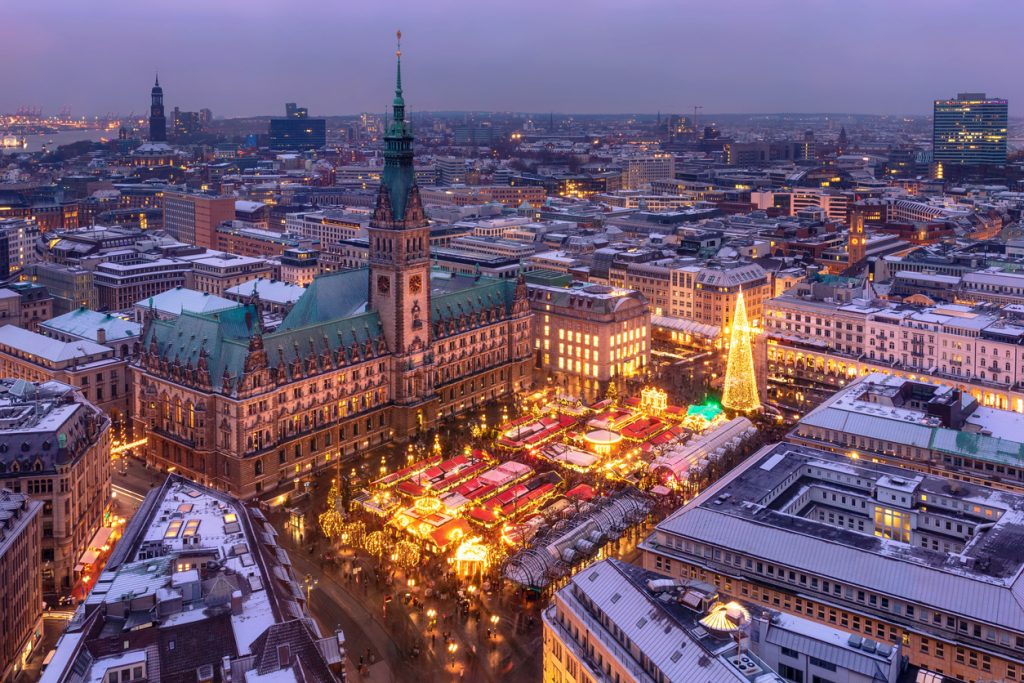 Das Hamburger Rathaus und der Weihnachtsmarkt leuchten in der Abenddämmerung.