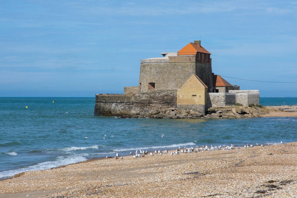 Alte Steinfestung am Meer nahe Maó auf Menorca, davor ein Kiesstrand mit Möwen.