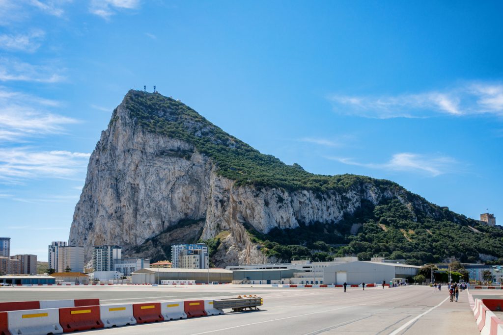 Blick über die Landebahn des Flughafens von Gibraltar auf den steilen Felsen mit grüner Vegetation.