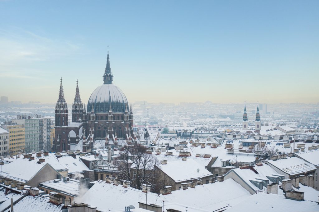 Blick auf eine große Kirche und schneebedeckte Dächer in Wien an einem klaren Wintertag.