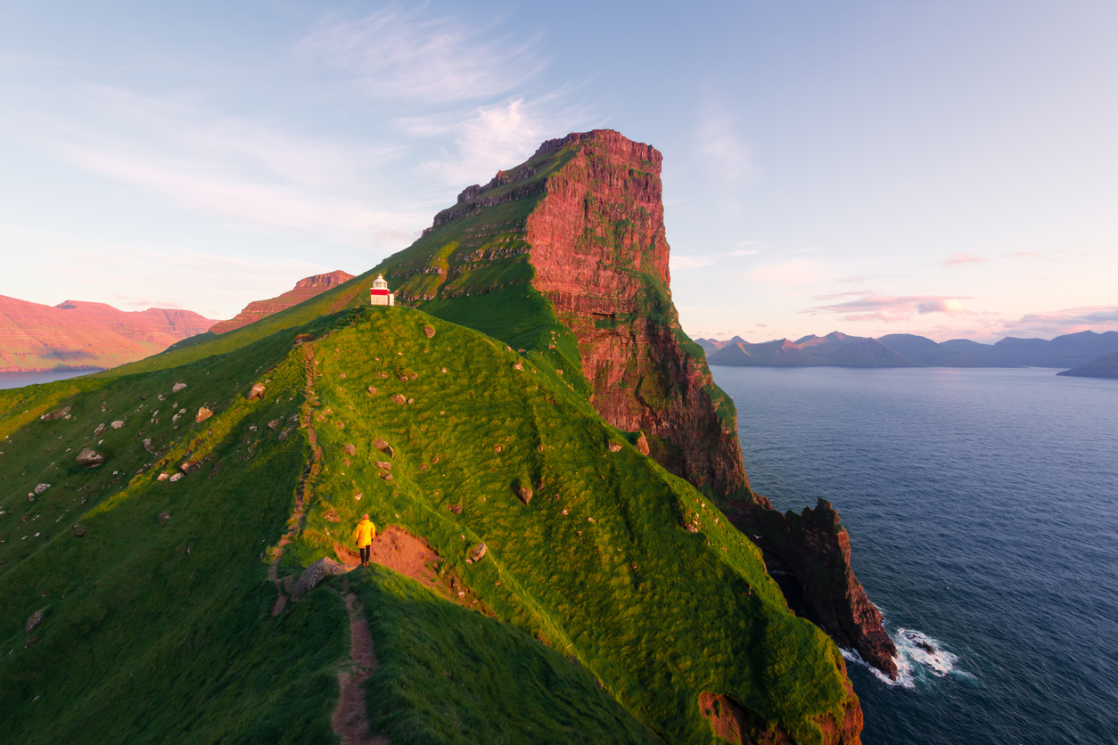 Wanderer geht auf schmalem Grat zum Kallur Leuchtturm auf den Färöer Inseln.