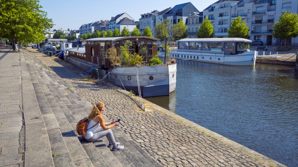 Am Ufer eines Kanals in Nantes liegen Hausboote, während eine Frau auf den Stufen sitzt.