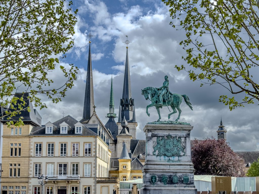 Reiterdenkmal in Luxemburg Stadt vor markanten Kirchtürmen und historischen Fassaden.