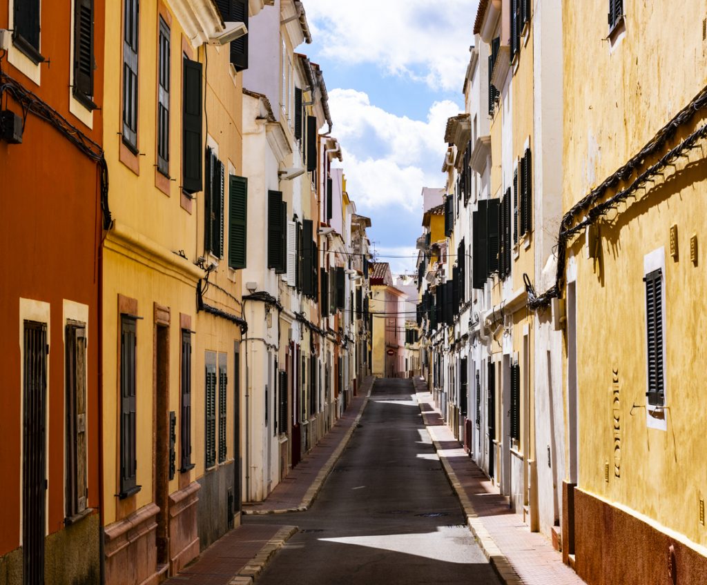 Schmale Straße mit farbigen Häusern und grünen Fensterläden in Maó auf Menorca.