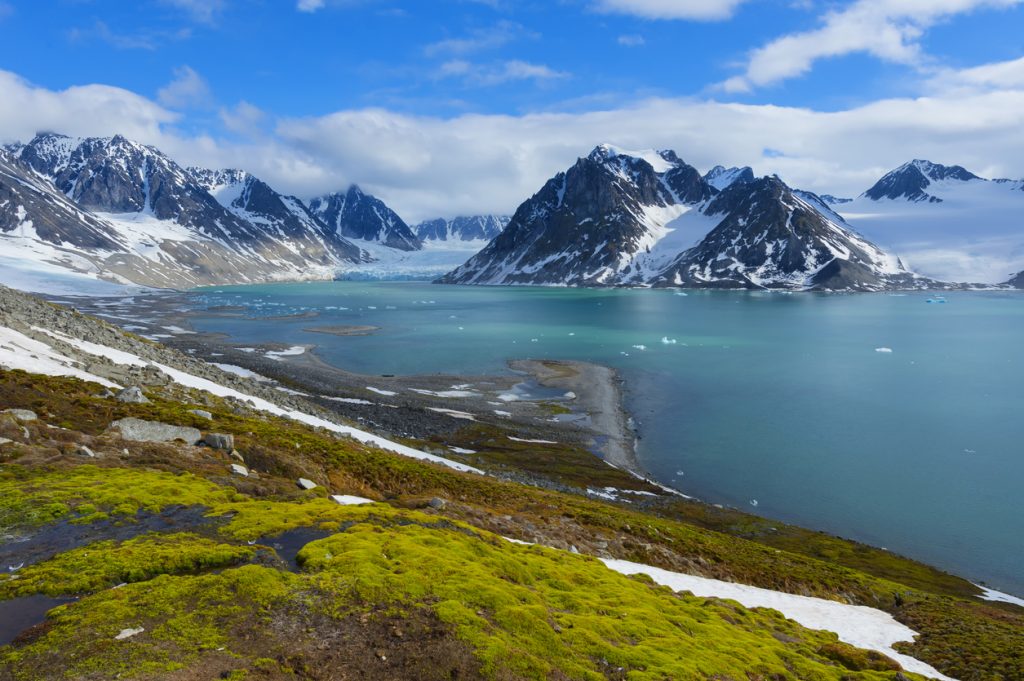 Ein türkisfarbener Fjord mit Gletscher ist von schneebedeckten Bergen auf Spitzbergen umgeben.