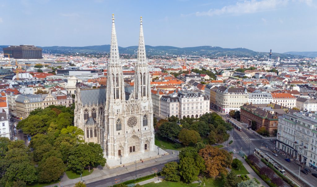 Aerialaufnahme der Votivkirche in Wien mit ihren zwei schlanken Türmen und den umliegenden Häusern.