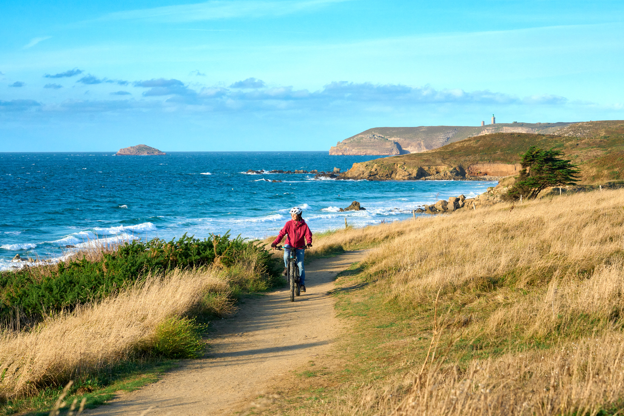 Ein Radfahrer fährt auf einem schmalen Küstenweg mit Blick auf das blaue Meer in der Bretagne.