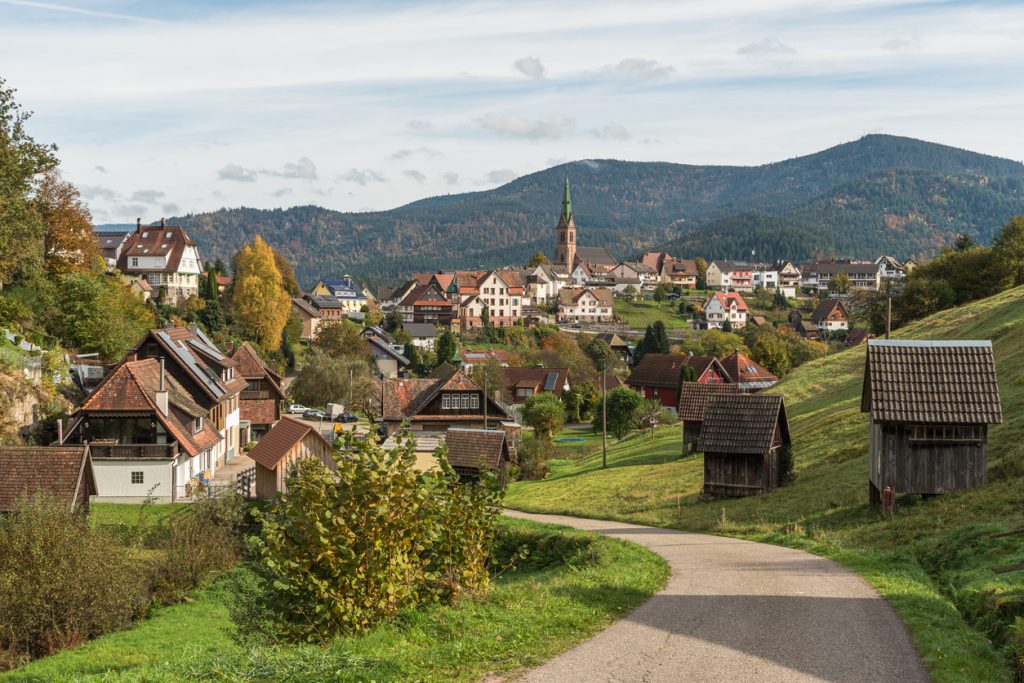 Dorf mit Fachwerkhäusern und Kirche liegt eingebettet in die Hügel des Schwarzwalds.