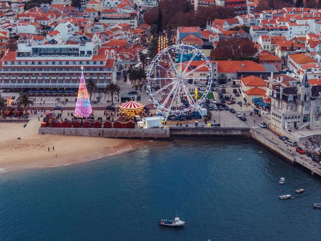 Eine portugiesische Küstenpromenade zeigt im Winter einen Weihnachtsmarkt mit Riesenrad direkt am Strand.