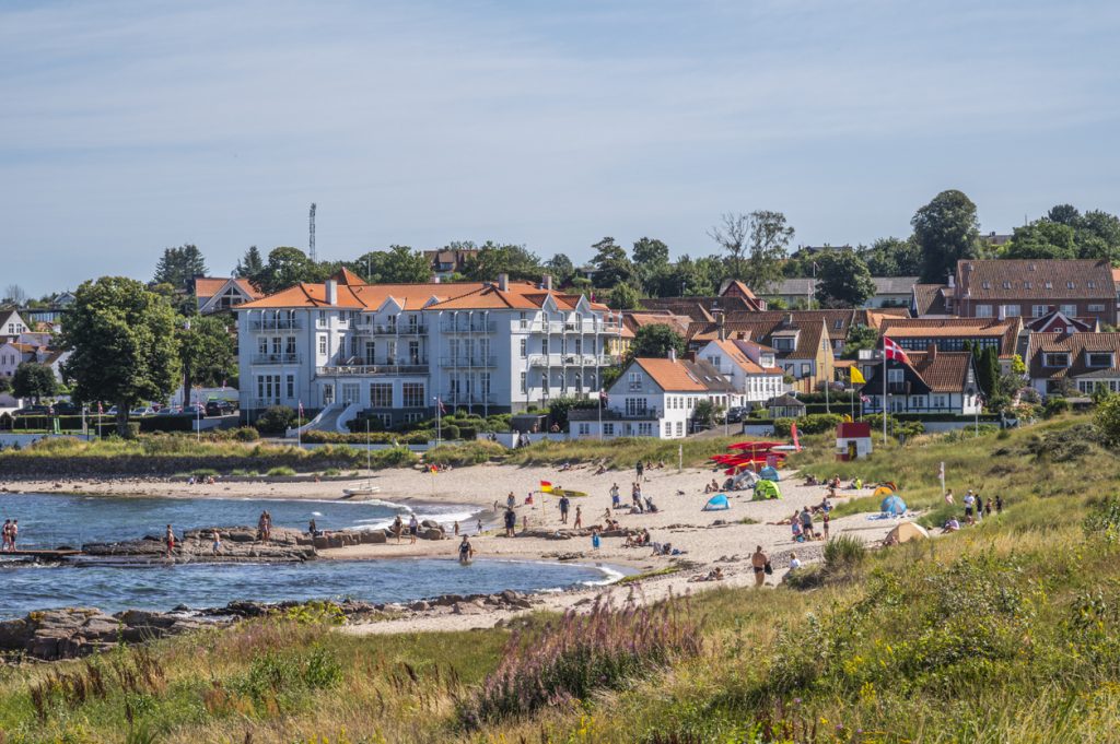 Sandstrand mit Badenden und Küstenort auf Bornholm im Sommer.