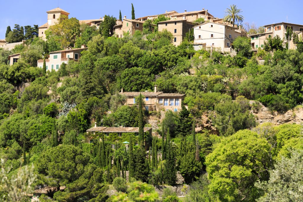 Steinfarbene Häuser von Banyalbufar liegen eingebettet in dichtes Grün am steilen Hang.