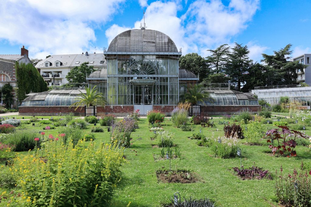 Das große Gewächshaus im Jardin des Plantes in Nantes steht hinter bunten Blumenbeeten.