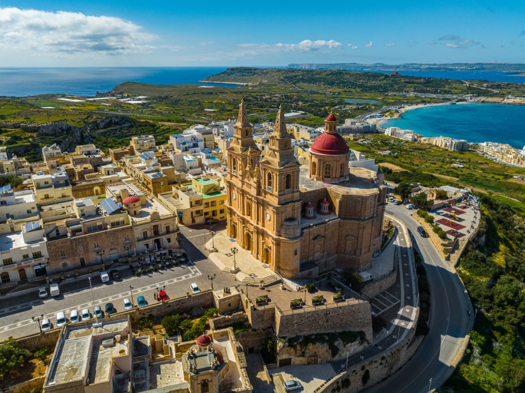 Luftaufnahme von Mellieħa auf Malta mit großer Kirche und Blick aufs Meer.