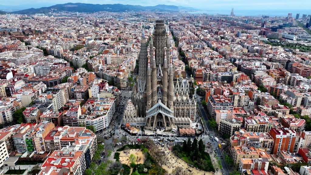 Luftaufnahme der Sagrada Família in Barcelona, umgeben von dicht bebauten Straßenzügen.