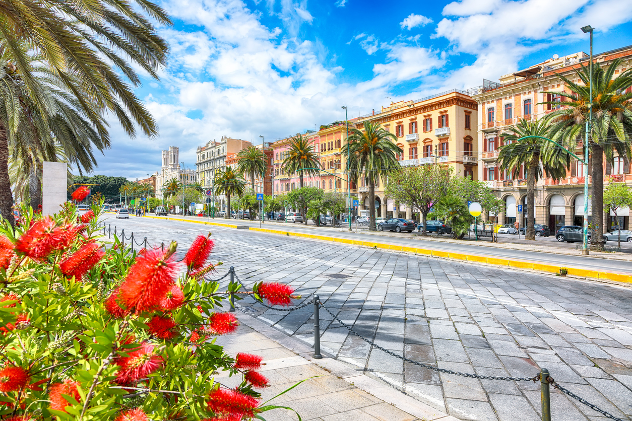 Bunte Häuserfassaden und Palmen säumen eine breite Straße in Cagliari