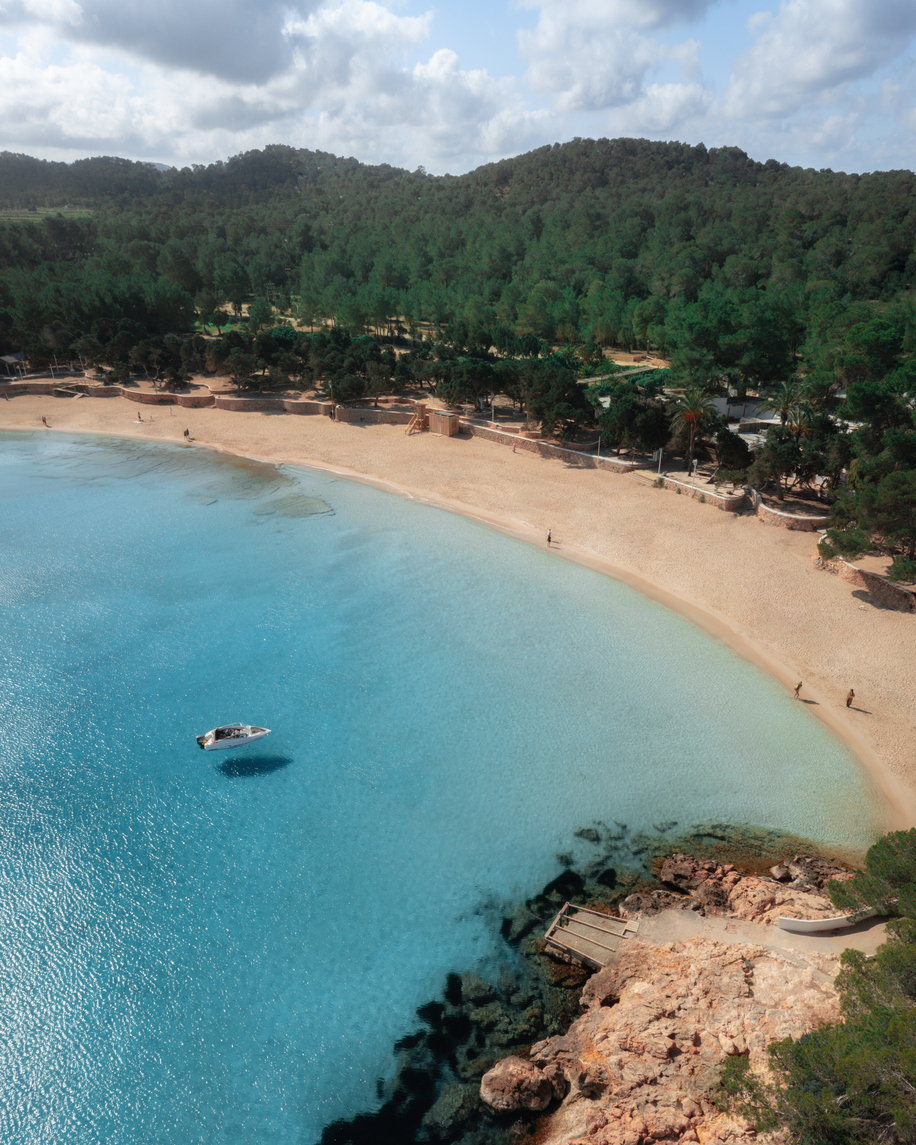 Blick auf die Cala Bassa mit hellem Sandstrand, flachem Wasser und einem Boot in der stillen Bucht.