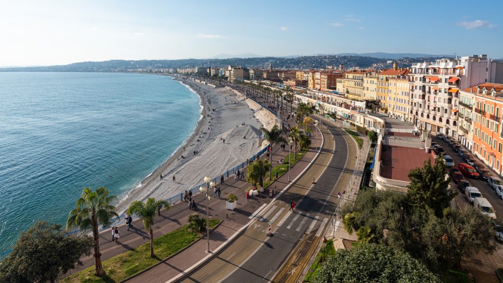 Luftaufnahme der Promenade des Anglais in Nizza mit Strand, Meer und Häuserzeile an der Côte d’Azur.